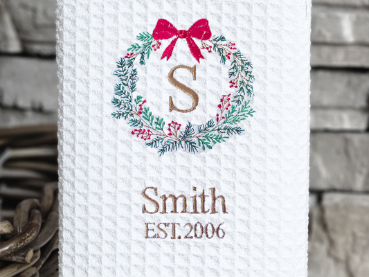 White towel with a decorative monogram and text on a stand against a stone wall.